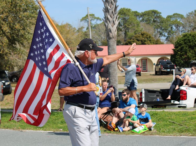Man holding American Flag leading Camp Gordon Johnston Days Parade