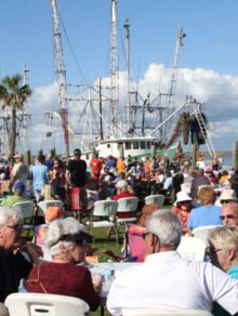 Crowd of people enjoying the sun and water by a shrimp boat at the Oyster Cook-Off in Apalachicola