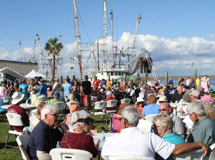 Crowd of people enjoying the sun and water by a shrimp boat at the Oyster Cook-Off in Apalachicola